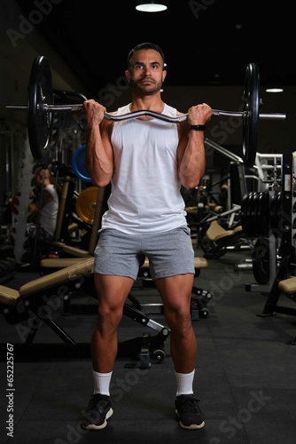 Strong Hispanic man doing barbell curl for biceps strength at a gym.