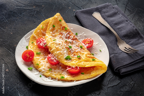 An omelet with tomato and parsley, eggs for breakfast, a healthy vegetarian dish with cheese, on a black slate background, with a fork