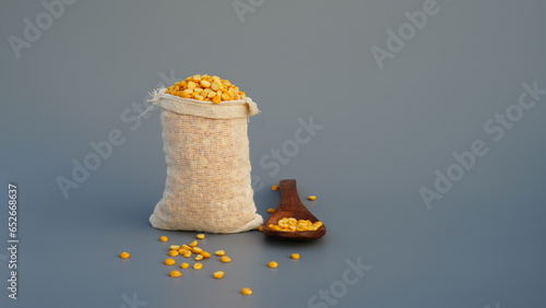 Studio close up of Organic Bengal Gram in burlap sacks, Cicer arietinum or split yellow chana dal with wooden spoon cleaned on a gray background. Front view