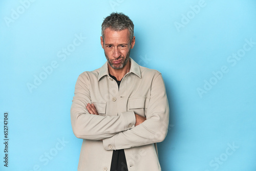 Middle-aged caucasian man on blue backdrop unhappy looking in camera with sarcastic expression.