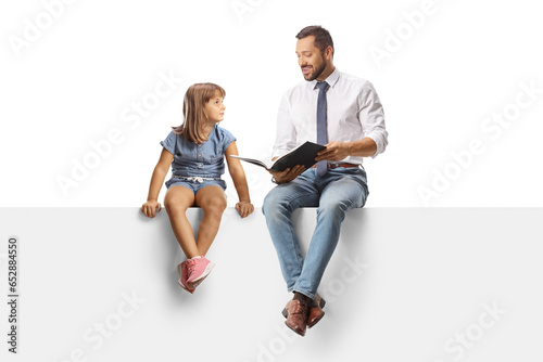 Man reading a book to a little girl and sitting on a blank panel