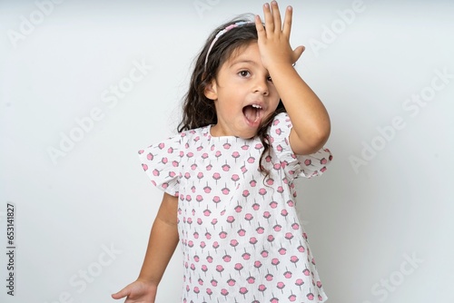 beautiful kid girl wearing dress surprised with hand on head for mistake, remember error. Forgot, bad memory concept.