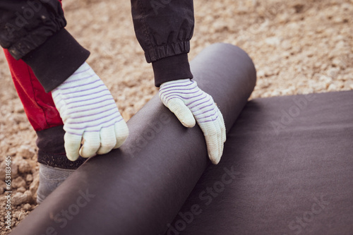 A woman spreads a roll of black agricultural fiber on the ground