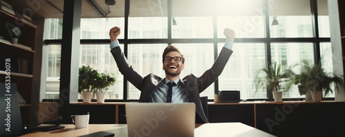 Successful businessman sitting in his office and raising his hands up.