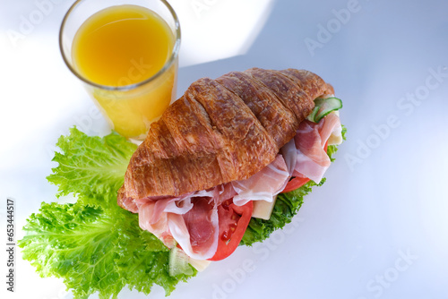 croissant sandwich with meat jamon prosciutto with tomato Lettuce leaves vegetables natural healthy expensive food rich pieces of cheese in breakfast France on a white plate. expensive restaurant