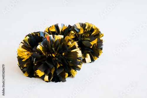 Gold and black cheerleading pom-poms on white practice mat