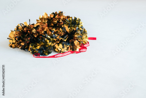 Gold and black pompoms with a red cheerleading ribbon on a white practice mat. Background