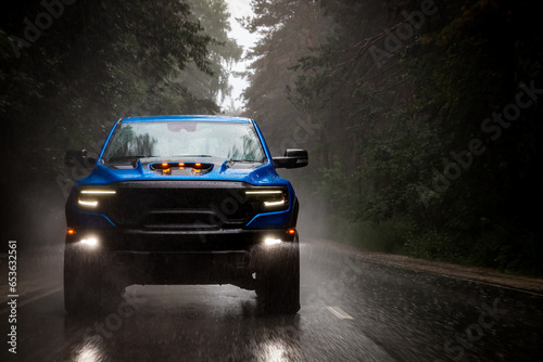 A blue new pickup truck is driving along a highway in the forest with a blurred background. Fast driving