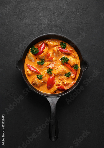 Chicken paprikash dish with paprika, onion, sweet pepper in black pan on dark table. top view
