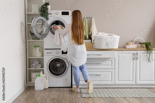 Woman putting dirty clothes into washing machine in laundry room