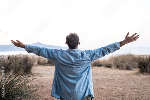One man standing outdoor outstretching arms in front of nature view landscape and clear sky. Concept of freedom and travel, healthy lifestyle balanced mental condition. Tourist enjoying destination