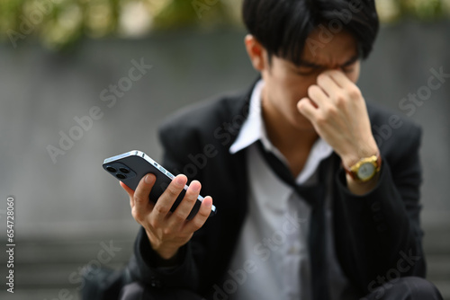 Stressed businessman using smartphone while on stairs of office building, loss of work during the recession