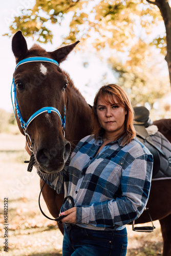 Woman holds a horse by the reins. Horseback riding in the autumn forest. Rental