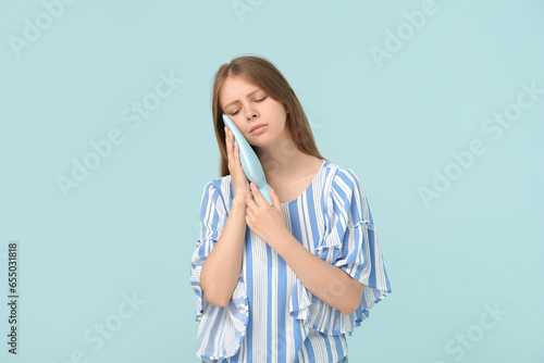 Young woman with tooth ache holding cold compress on blue background