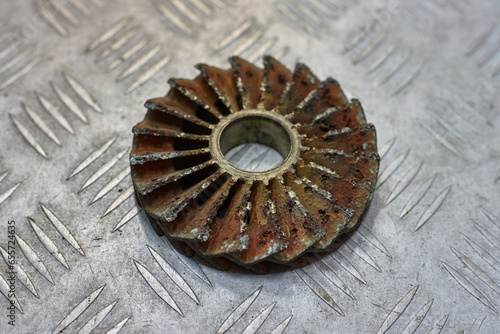 Bronze centrifugal pump impeller worn out by cavitation on metal table.