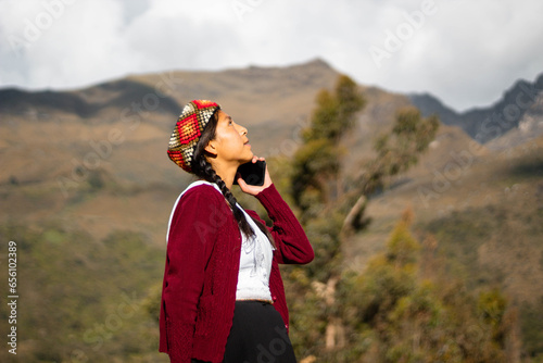 Foto de una feliz campesina caucásica hablando por teléfono inteligente puesta una chopa tejido a mano .campesina con ropa típica artesanía peruana a mano en un atardecer en los Andes peruanos. Mujer