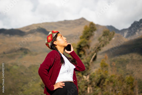 Foto de una feliz campesina caucásica hablando por teléfono inteligente puesta una chopa tejido a mano .campesina con ropa típica artesanía peruana a mano en un atardecer en los Andes peruanos. Mujer