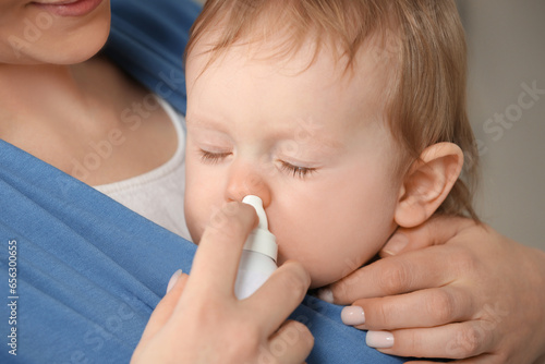 Mother helping her baby to use nasal spray, closeup