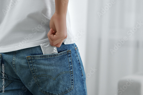 Man pulling condom out of pocket indoors, closeup. Space for text