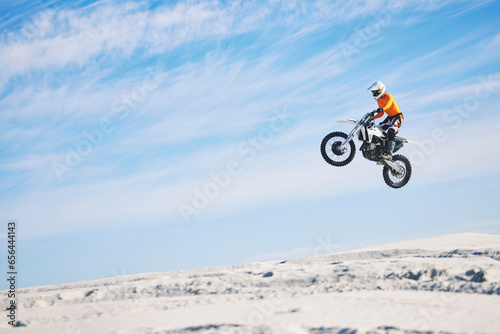 Motorcycle, desert and jump for sports in race, adrenaline and training for fitness in competition. Athlete, sky and mockup for freedom, driving and dirtbike in outdoor for stunt or performance