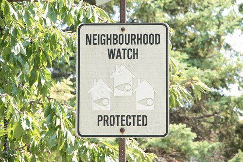 neighbourhood watch protected writing caption text rectangle sign on post with tree behind and faced picture illustrations of homes houses with eyes on in them, black and white