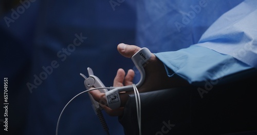 Male patient lies on table under anesthesia in surgery room. Surgeons perform difficult operation. Close up of hand of man with medical sensors and pulse meter. Modern equipment in clinic or hospital.