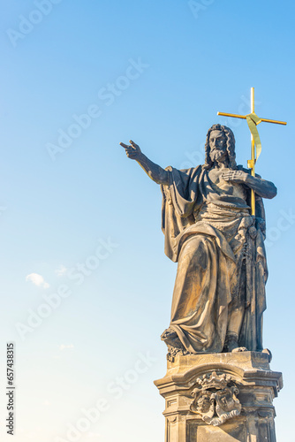 Cover page with ancient statue of Saint John of Nepomuk with cross at the Charles Bridge in Prague at blue sky sunset colors and sunlight, Prague, Czech Republic.
