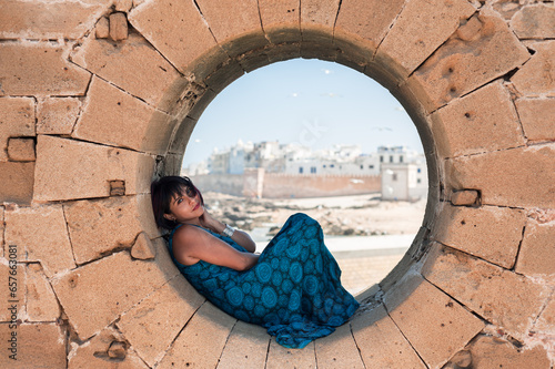 Attractive South American Girl Posing In A Resting Moment In A Circular Hole In A Fortress Wall While Traveling In Essaouira, Morocco.JPG