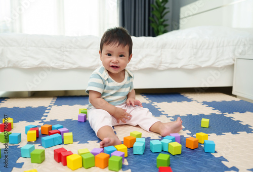 happy infant baby playing wooden block toy on jigsaw mat in bedroom