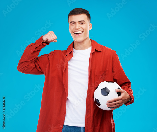 Portrait, football and happy man with strong muscle in studio isolated on a blue background. Face, soccer and excited person flex bicep for power, sports and success in competition, winner or fitness