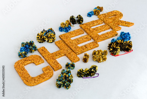 Large gold letters "CHEER" on a white training mat surrounded by cheerleading pom-poms in different colors