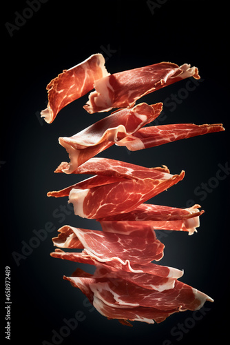 Thin slices of Spanish ham jamon flying in the air on black background. Traditional meat specialty of the local cuisine