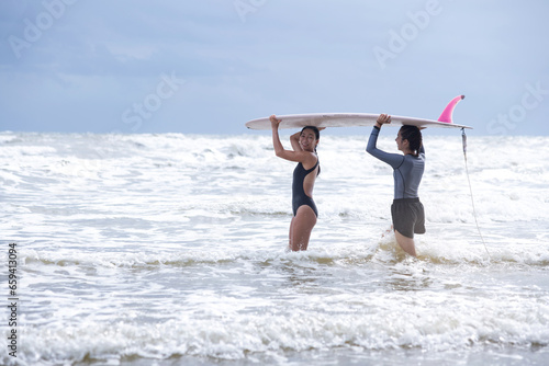 Pretty teen girl and her instructor carry a surfboard on head into the sea, the first lesson to start surfing in the sea, women and outdoor sports