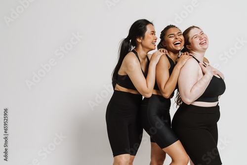 Three joyful women in sportswear posing together isolated over white background