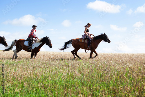 Horseback riding. Horseback riding. Young women equestrians gallop on horses through a field on a summer sunny day.