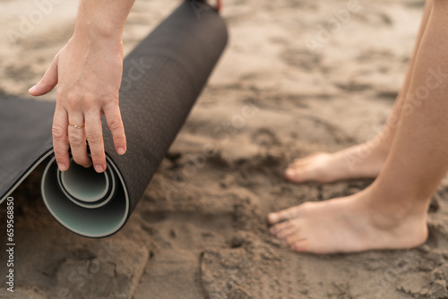 hands of a young lady unrolling a yoga mat at the beach after the sunrise