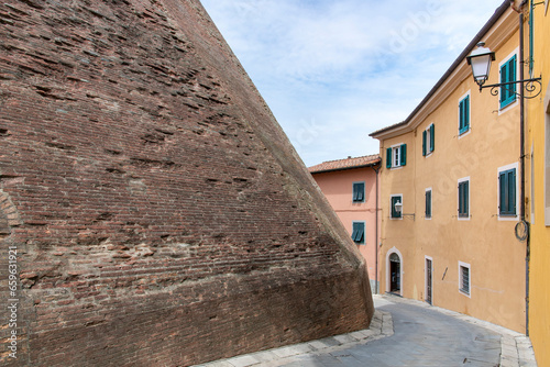 Street in town of Lari, Italy lined with historic houses with plastered colorful walls and the fortified brick wall of the Castle of Lari (Castello dei Vicari)