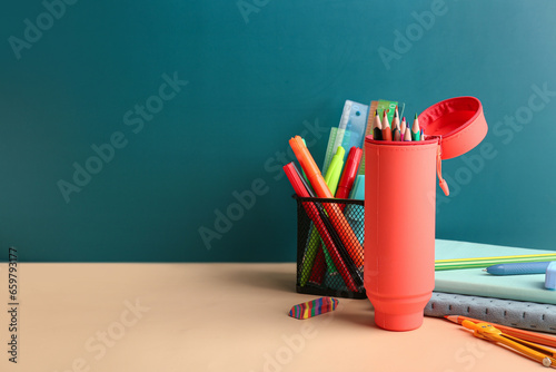 Red pencil case with school stationery on school desk near blackboard