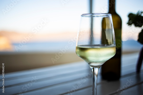 White wine served on a wineglass with bottle and cork on a wooden table in Mediterranean landscape background in Santorini, Greece