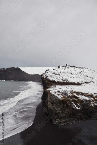 Stunning black sand beach in Iceland with snow-covered cliffs, silhouetted people on mountains