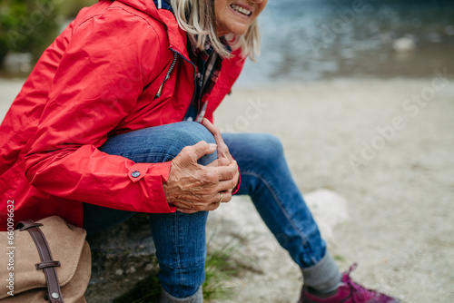 Senior woman injured leg during hike in the mountains. Tourist went off-trail and fell. Eeeling pain under kneecap, also known as Hiker's knee.