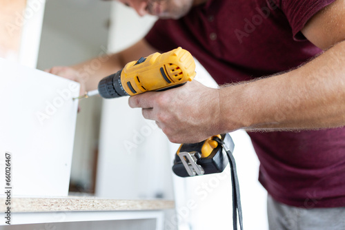 Man worker assembling kitchen wooden elements with cordless screwdriver drill.