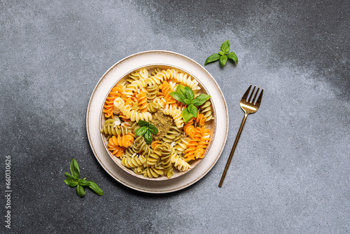 Colorful full grain fusilli pasta with homemade pesto sauce and fresh basil leaves on gray stone background top view.
