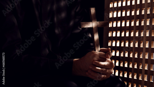 Young priest with cross in confession booth