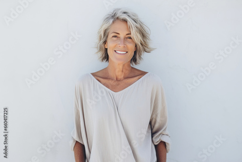 Smiling 60 year old woman standing in front of an outdoor wall.
