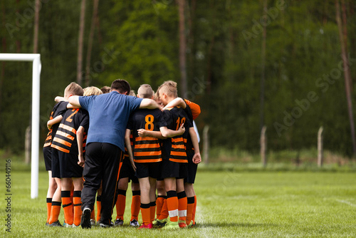 Group of school boys huddling united in soccer team before tournament football match. Boys in sports uniforms standing in a circle with coach