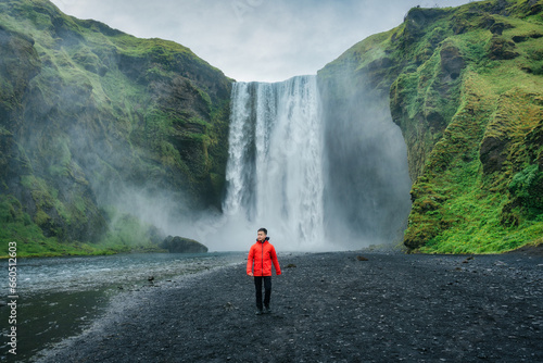 Powerful Skogafoss waterfall and male tourist walking in summer at Iceland