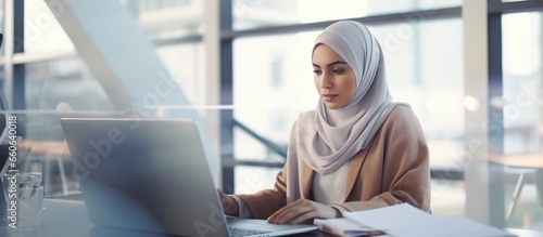 Young businesswoman in hijab sitting at desk in office working online with laptop. Muslim woman working in the office.