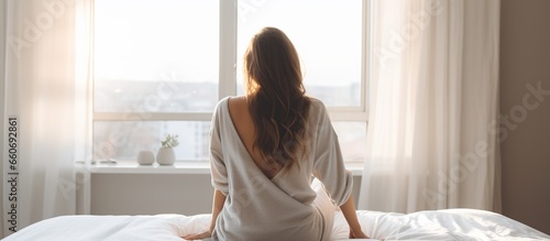 Rear view of young beautiful woman looking at the window after waking up