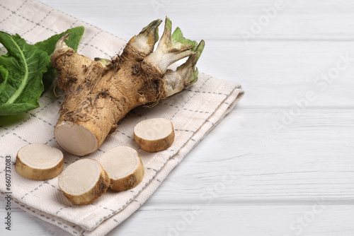 Cut horseradish root and leaves on white wooden table, closeup. Space for text
